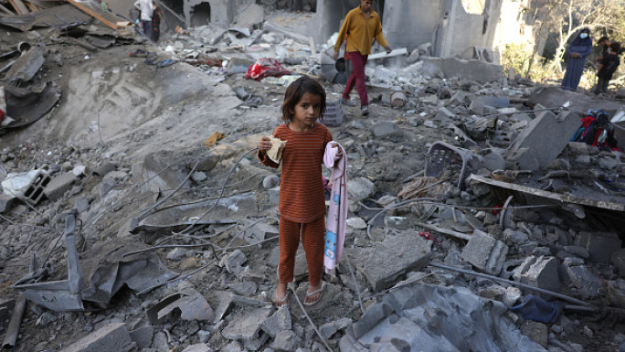  A girl eats a piece of bread as people check the site of an overnight Israeli strike, in Jabalia in the central Gaza Strip, on May 30, 2025